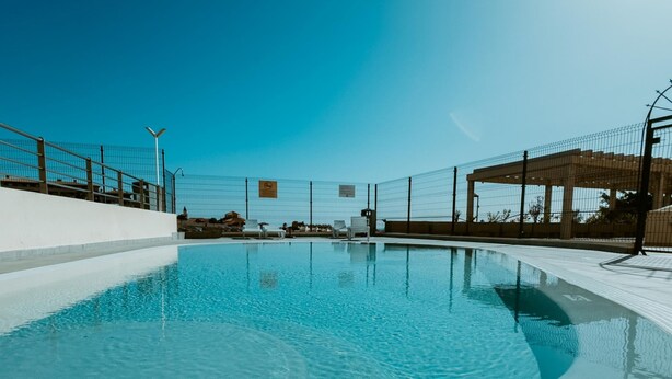 A clear blue swimming pool with a tiled deck, surrounded by a fence and a covered area. - Seaview Splendor 2 Bedroom Modern Comfort (Adeje)