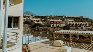 A hotel with a pool area, outdoor seating, and a view of other buildings and a mountain in the background. - Seaview Splendor 2 Bedroom Modern Comfort (Adeje)
