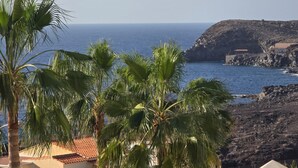 A coastal view with palm trees, a rocky shoreline, and a building with a red roof. - Sun Kissed Vacation Home 3BR Retreat by the Ocean (Adeje)