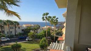A balcony with a view of a coastal area, including buildings, palm trees, and the sea. - Sun Kissed Vacation Home 3BR Retreat by the Ocean (Adeje)