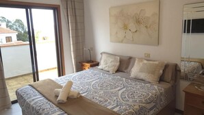 Ein Schlafzimmer mit einem großen Bett, einem Nachttisch, einem Spiegel und Blick ins Freie.