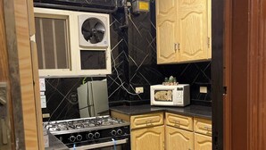 A compact kitchen with a gas stove, oven, microwave, and wooden cabinets. - Dokki apartment  (Giza)