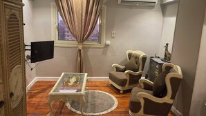 A living room with a television, two armchairs, a glass coffee table, and a window with curtains. - Dokki apartment  (Giza)