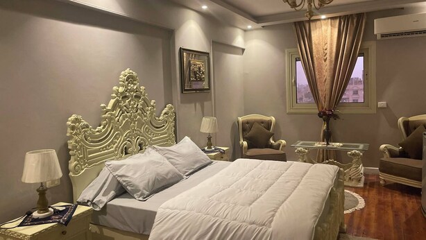 A bedroom with a large bed, a chandelier, a chair, and a small table with a vase. - Dokki apartment  (Giza)