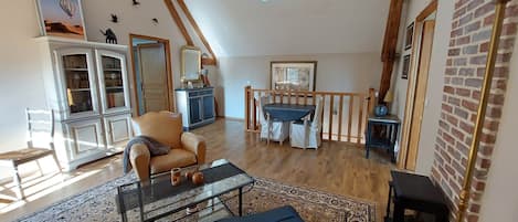 A spacious living room with a high ceiling, wooden beams, a dining area with a table and chairs, and a fireplace.