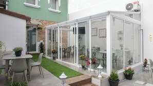 A conservatory with glass walls, a patio area with chairs and tables, and potted plants. - Terra de Padrón Quality Rooms (Padron)