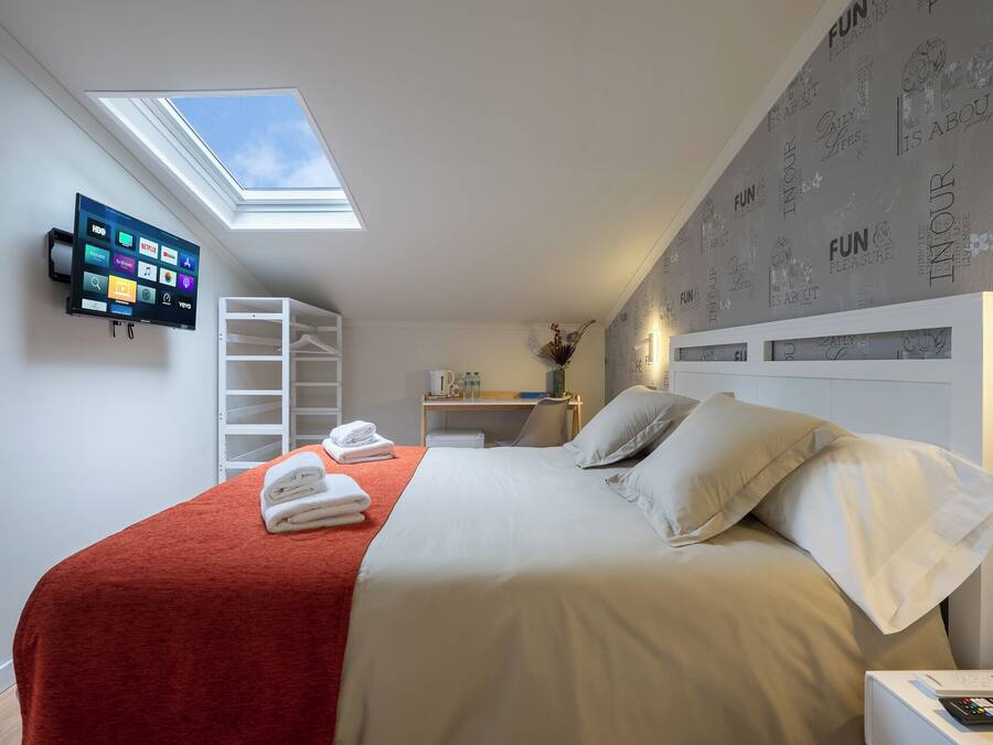 Un dormitorio moderno con tragaluces, una cama con sábanas blancas, un escritorio con silla y un televisor de pantalla plana montado en la pared.