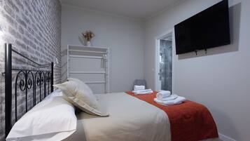 Un dormitorio con cama, almohadas, una colcha roja, un televisor montado en la pared y un armario.