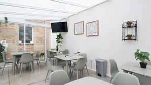 A modern, well-lit room with a stone wall, a flat-screen TV, and several tables and chairs. - Terra de Padrón Quality Rooms (Padron)