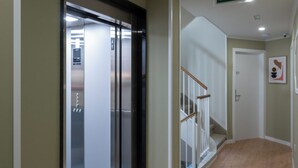 A hallway with a sliding glass door leading to a room, a staircase with a white railing, and a green emergency exit sign on the wall. - Terra de Padrón Quality Rooms (Padron)