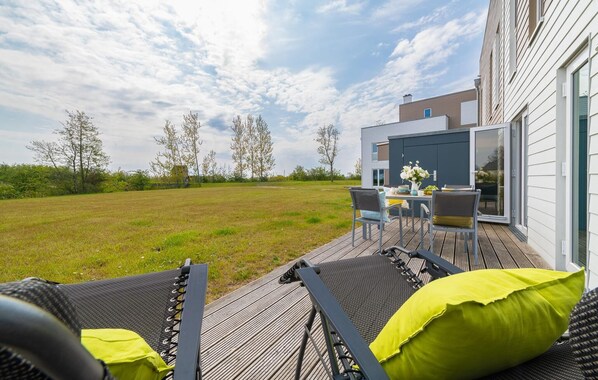 Een terras met buitenmeubilair, een tafel en stoelen, met uitzicht op een gazon en een modern gebouw met grote ramen.