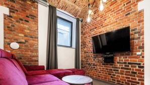 A modern living room with a brick wall, a large flat-screen TV, a red sofa, and a small round table.
