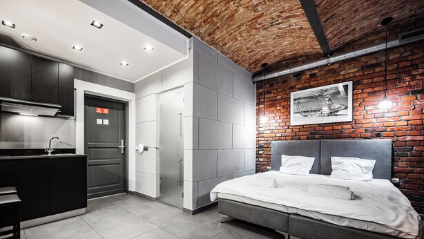 A modern bedroom with a large bed, a built-in wardrobe, and a kitchen area.