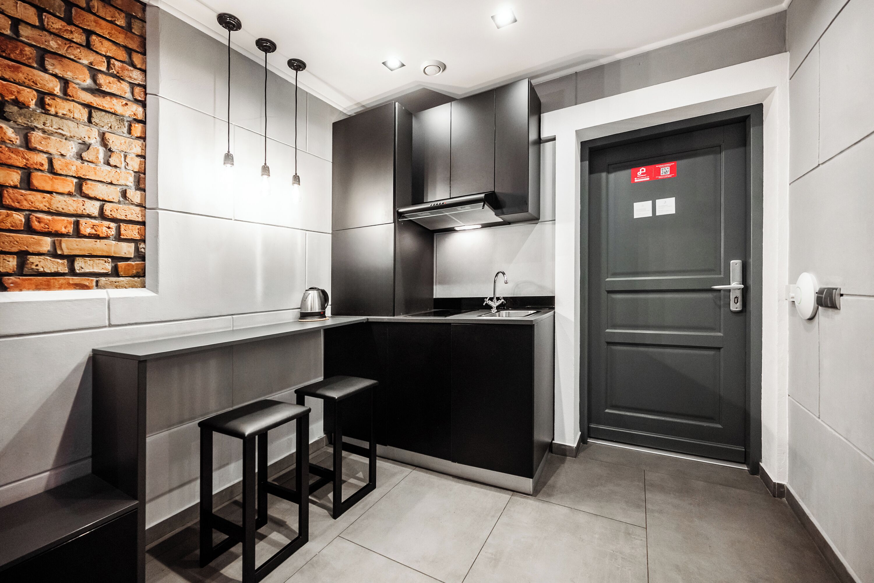 A modern kitchen with a brick accent wall, a built-in stove, and a dark door with a red sign.