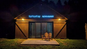A wooden building with a sloped roof and large glass doors, a bench outside, and illuminated signage above. - Romantic Getaway near Whiteface (Upper Jay)