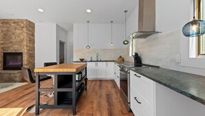 A modern kitchen with white cabinets, a wooden dining table, and a built-in fireplace. - Romantic Getaway near Whiteface (Upper Jay)
