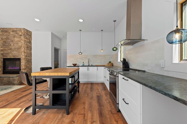 A modern kitchen with white cabinets, a wooden dining table, and a built-in fireplace. - Romantic Getaway near Whiteface (Upper Jay)