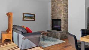 A modern living room with a stone fireplace, a sofa, a wooden side table, and a dining area. - Romantic Getaway near Whiteface (Upper Jay)