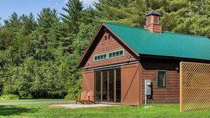A wooden cabin with a green roof, large sliding glass doors, and a chimney. - Romantic Getaway near Whiteface (Upper Jay)