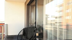 A balcony with a black chair and a small table with a lamp.