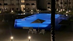 Ein Schwimmbecken bei Nacht mit umgebenden Gebäuden und einem Weg.