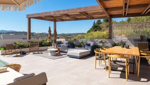 Una terraza en la azotea con un pérgola de madera, asientos exteriores, una piscina y vistas del paisaje.