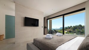 Un dormitorio moderno con una cama grande, un televisor de pantalla plana montado en la pared y vistas a un paisaje montañoso a través de un ventanal amplio.