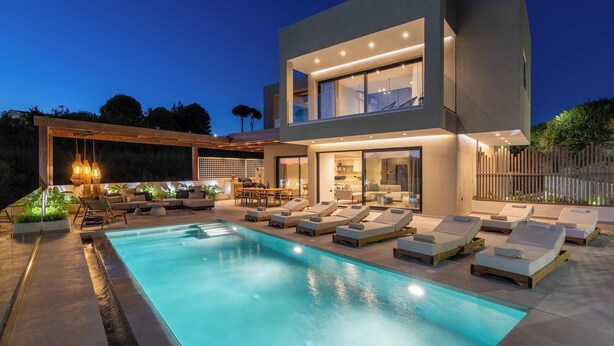 Una casa moderna de dos pisos con piscina, mobiliario exterior y un patio bien iluminado.