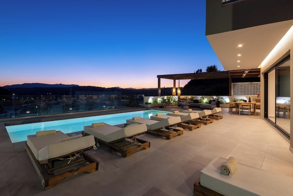 A rooftop pool area with sun loungers, a seating area, and a view of the mountains.