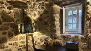 A stone-walled room with a desk, a lamp, a small potted plant, and a window. - an accommodation unit in the form of a studio T1 with 39m2 (Sortelha)