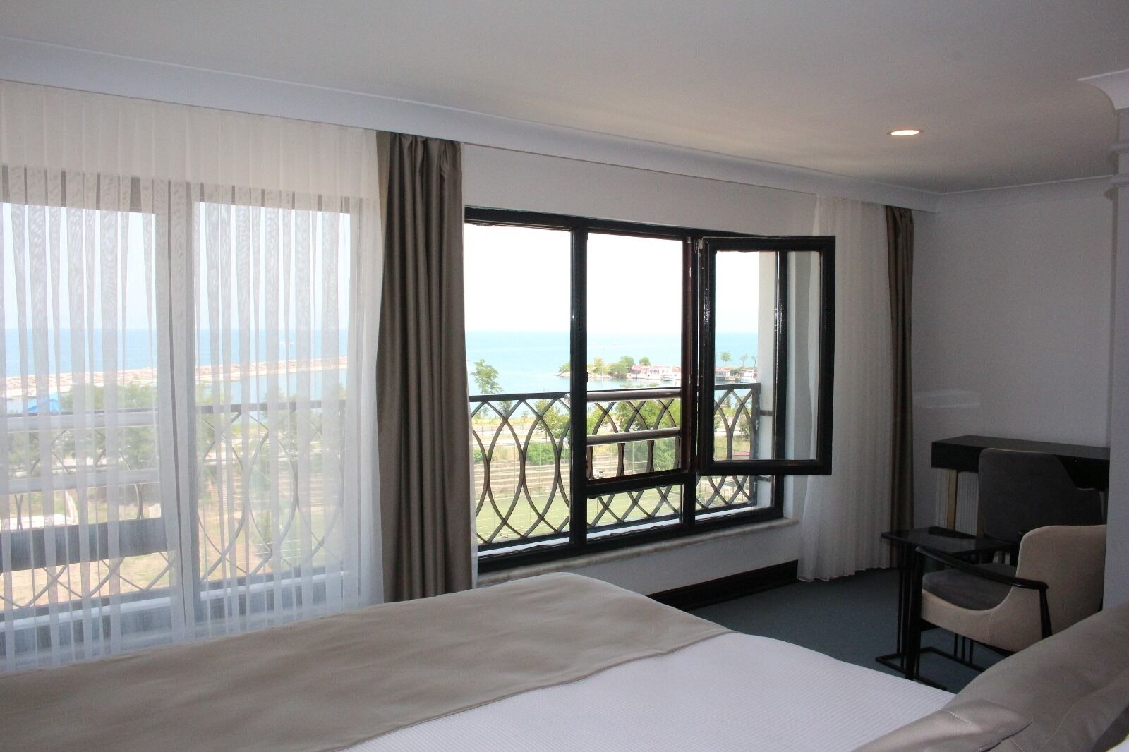 Habitación de hotel con una cama grande, un escritorio y vistas al mar y a edificios.