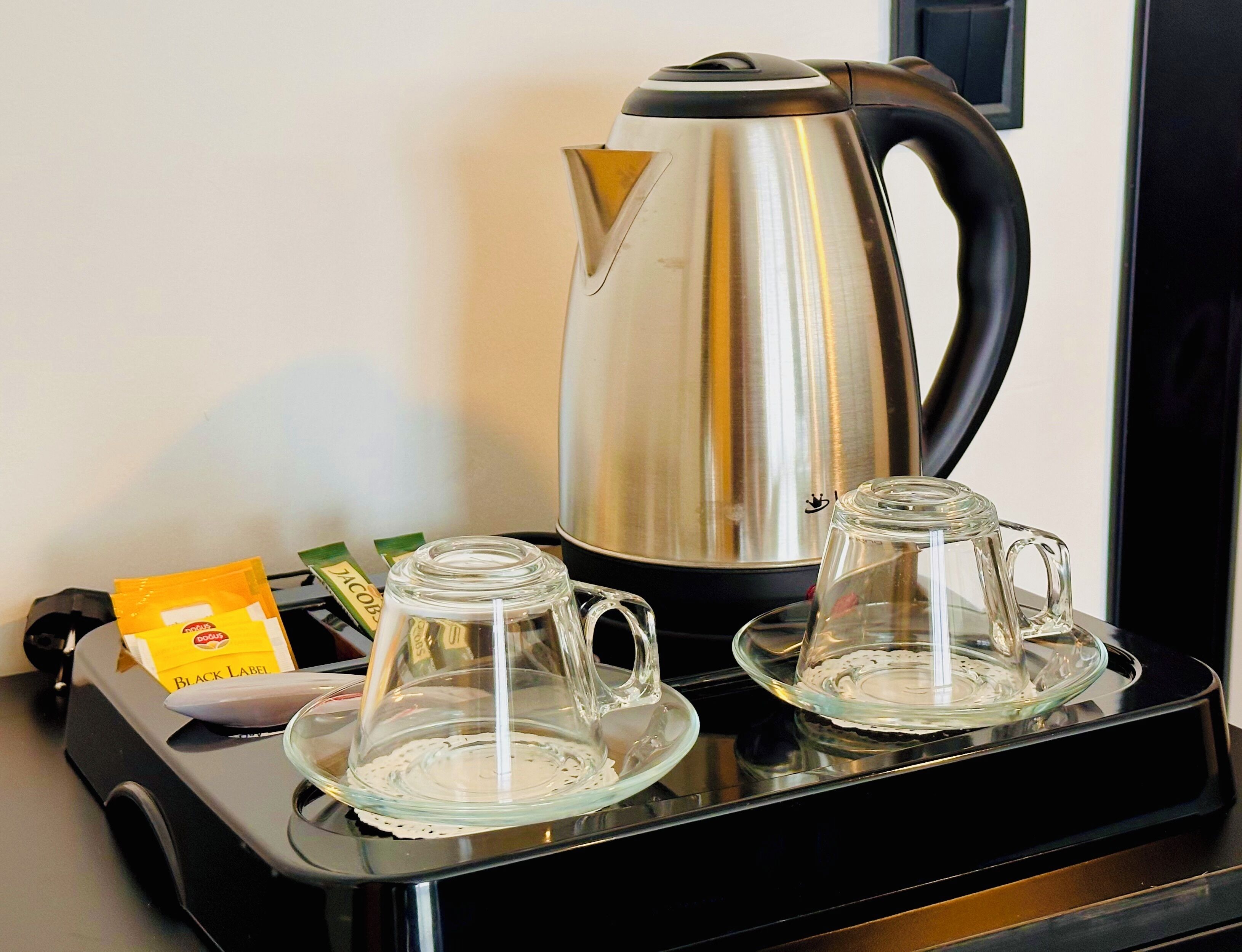 Ett köksutrymme med en vattenkokare i rostfritt stål, två glasmuggar på ett fat och en förpackning kaffe märkt med texten ”Black Label”.