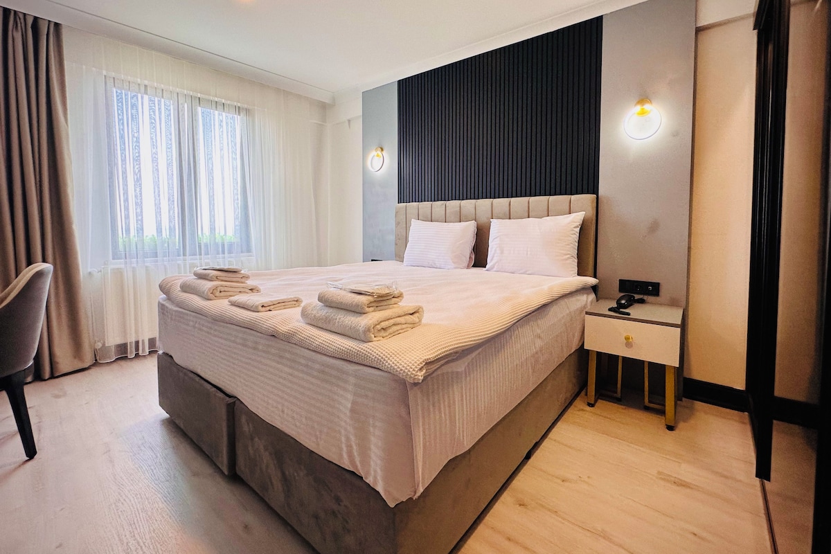 A modern hotel room with a large bed, bedside tables, and a chair.