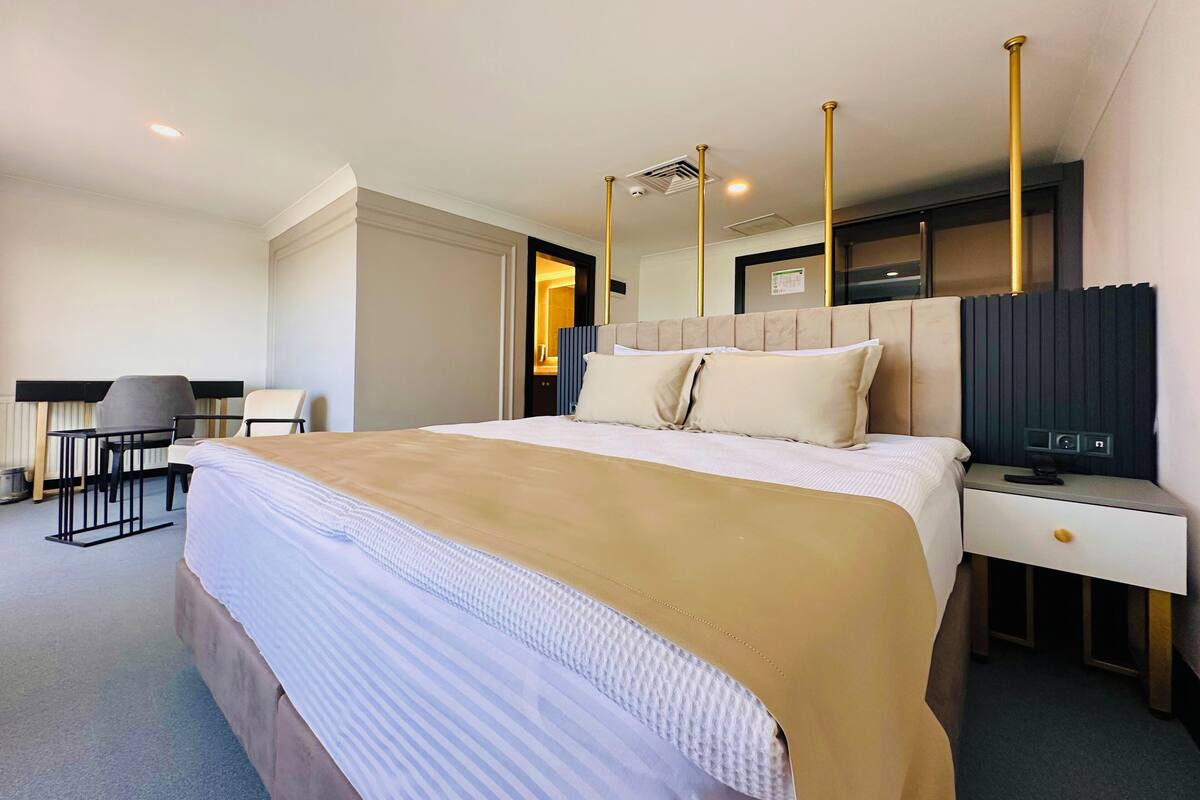 Ein Hotelzimmer mit einem großen Bett, einem Schreibtisch mit Stuhl, einem Fernseher und einem Nachttisch.