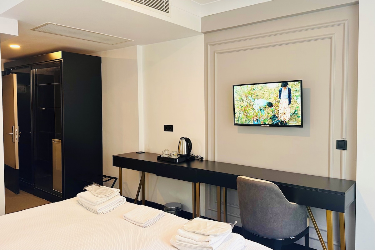 A hotel room with a bed, a desk with a flat-screen TV, a chair, and a wardrobe.