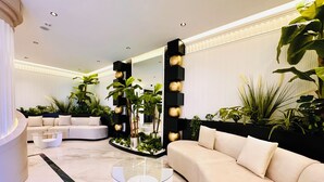 Ein modernes Wohnzimmer mit einem weißen Sofa, einem Glastisch und einer schwarzen Wand mit goldenen, kugelförmigen Verzierungen.