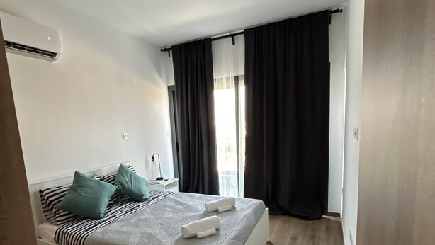A modern bedroom with a bed, a bedside table, a window with curtains, and a ceiling light. - Cozy 3 Bedroom Villa Close to the Beach (Limassol)