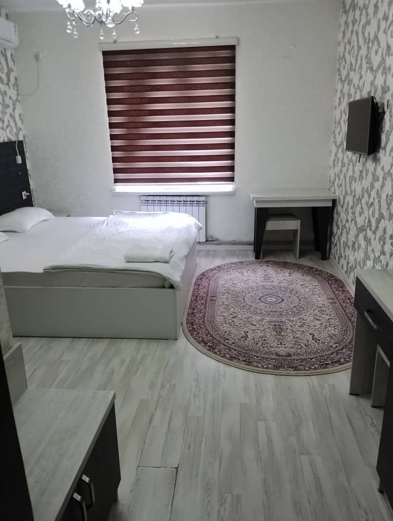 Ein Schlafzimmer mit einem Bett, einem Nachttisch, einem Teppich und einem Fenster mit Jalousien.