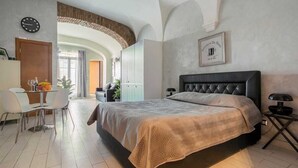 A modern bedroom with a large bed, a dining area with a table and chairs, and a kitchen visible through an archway.