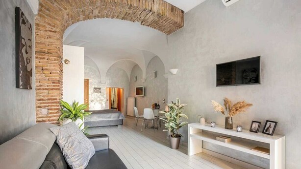 A modern living room with a brick archway, a sofa, a dining area, and a TV mounted on the wall.