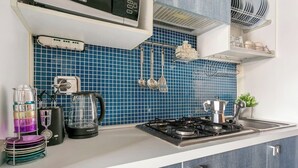 A modern kitchen with a gas stove, a coffee maker, and a kettle. There are utensils hanging on the wall and a dish rack.