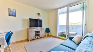 Ein Wohnzimmer mit Fernseher, einer Couch, einem Esstisch mit Stühlen und einem Balkon mit Aussicht.