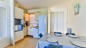 A compact kitchen with a microwave, stove, and refrigerator. There is a dining table set with plates, glasses, and cutlery. - La Goëlette 30 Les mouettes (Saint-Hilaire-de-Riez)