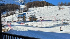 En snötäckt skidbacke med en lift, en skidstuga och ett berg i bakgrunden.