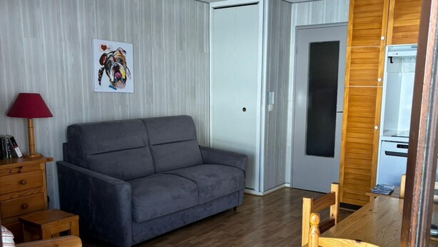 Ett vardagsrum med en grå soffa, trämöbler, ett träbord med stolar, en röd lampa och en tavla som hänger på väggen.