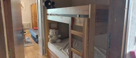 A bunk bed with a teddy bear on the lower bunk, a wooden wardrobe, and a bench in the room.