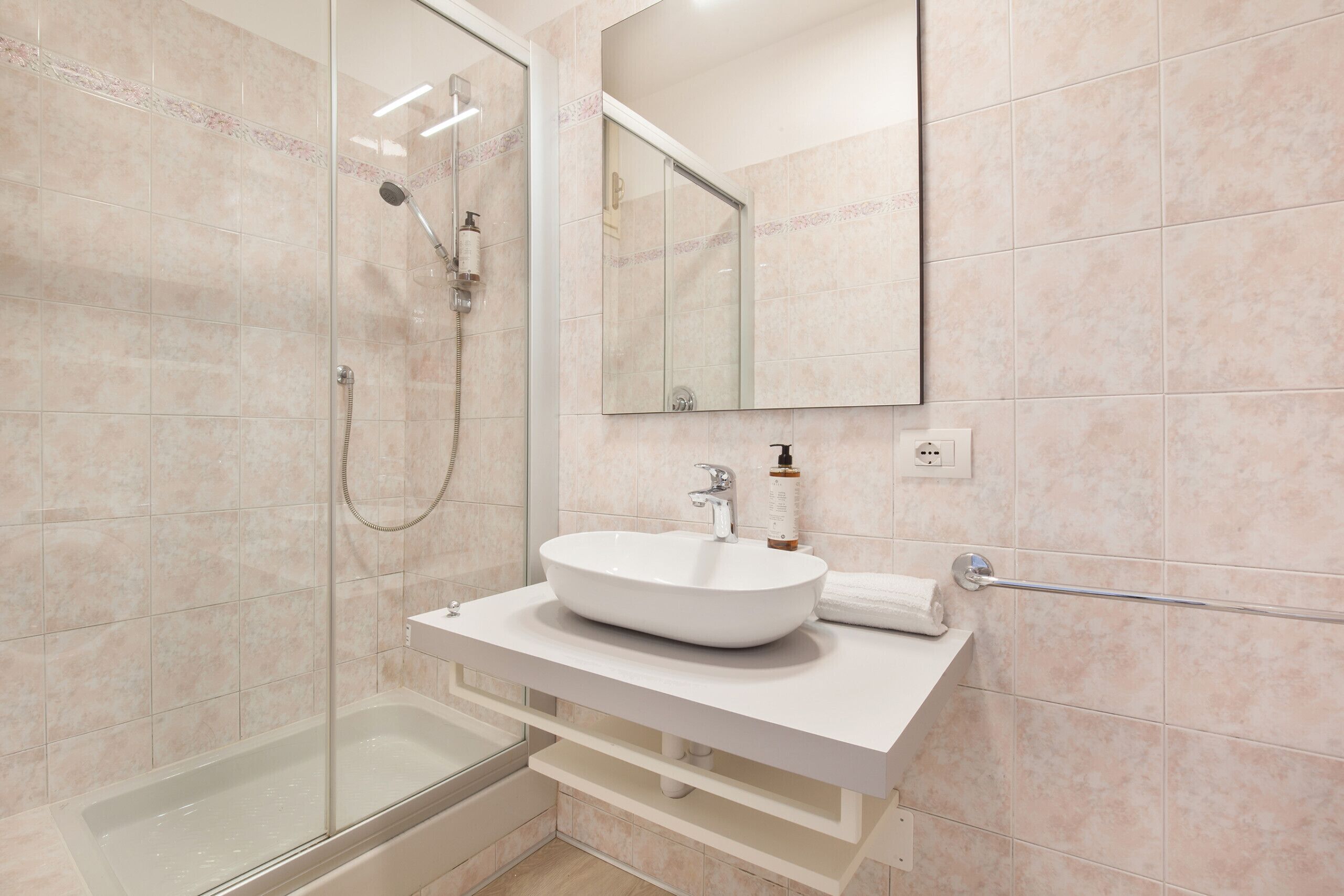 Une salle de bain moderne avec une douche à parois de verre, un lavabo blanc et un grand miroir au-dessus du meuble-lavabo.