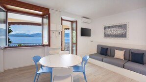 Una habitación con una mesa redonda, sillas azules, un sofá gris y vistas a un lago.