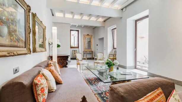 Un salon moderne avec une table basse en verre, un canapé marron agrémenté de coussins à motifs et un grand miroir.