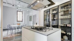 Une cuisine moderne dotée d’un îlot central, d’un coin repas avec des chaises transparentes et d’un meuble vitré où sont exposés les ustensiles de cuisine.